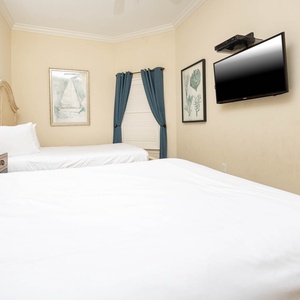 This cozy guest bedroom features two queen beds, a wall-mounted TV, and beach-themed decor for a relaxing stay