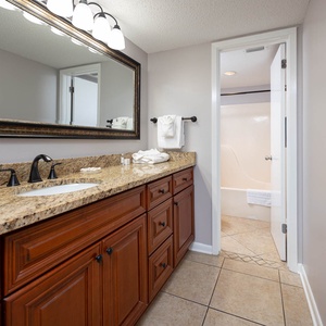 Elegant master bath featuring a spacious granite countertop, dark fixtures, and a tub/shower combo