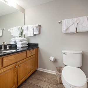 The guest bathroom features a dark countertop, ample white towels, and a glass shower enclosure for a refreshing experience