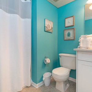 The guest bathroom features vibrant turquoise walls, a white shower curtain, and neatly stacked towels for a refreshing experience