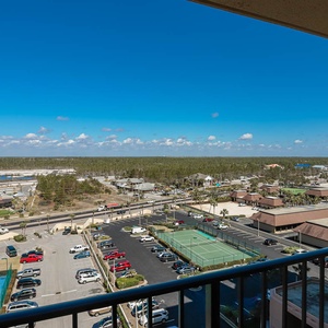 The balcony view showcases a vibrant landscape with tennis courts, parking areas, and a clear blue sky overhead