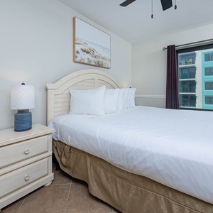 This bedroom features a comfortable bed with white linens, a stylish lamp, and a large window offering a view of the beach