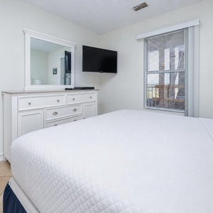 This cozy bedroom features a comfortable bed, a TV for entertainment, and a bright window offering a lovely view