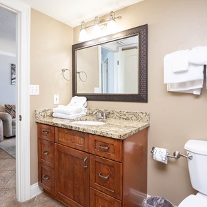Bathroom featuring a granite countertop vanity with neatly stacked towels, a large mirror, and a view into the living area