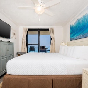 Unwind in the serene master bedroom with a large king bed, flat-screen TV, and access to the beachfront balcony
