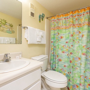 This bathroom features a fish-patterned shower curtain, a spacious vanity, and cheerfully refershing tropical décor