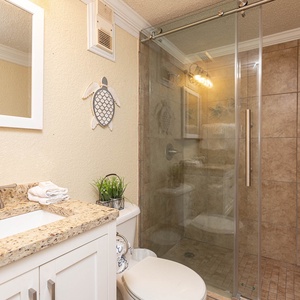 This bathroom features a stylish shower with glass doors, elegant granite countertops, and a relaxing coastal decor