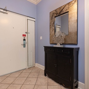 Step into a welcoming entryway featuring stylish decor, a sleek mirror, and a glimpse of the cozy bedroom beyond