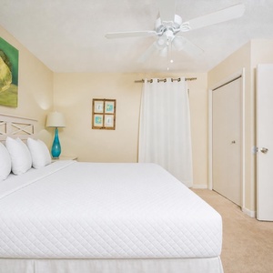 A serene bedroom features a large king bed with white linens, complemented by a colorful painting and a stylish lamp