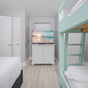 A cozy guest bedroom features a queen bed, a turquoise double bunk bed, and a TV on a white cabinet