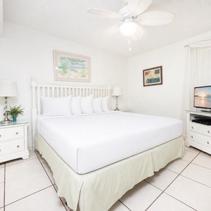 Bright bedroom featuring a large king bed, light-colored furnishings, and a TV, creating a serene and inviting atmosphere
