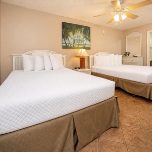 Guest bedroom featuring two queen beds, a ceiling fan, and tropical artwork, creating a relaxed vacation atmosphere
