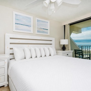 This bedroom features a plush white bed, stylish decor, and a stunning beachfront view from the large sliding glass doors