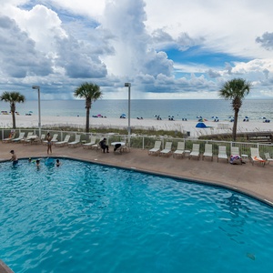 Enjoy a refreshing poolside experience with a view of the beach and colorful umbrellas in the distance