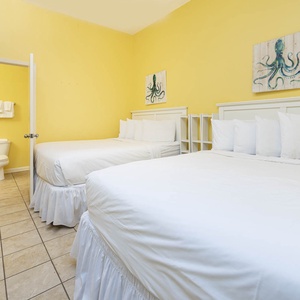 Bright yellow walls complement two queen beds with white linens, creating a cheerful atmosphere in this inviting guest room