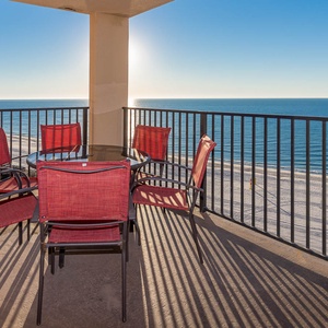 Enjoy dining on the balcony with a glass table and red chairs, overlooking the tranquil beach and sparkling water
