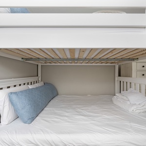 Spacious queen bunk bed with a soft blue accent pillow, perfect for family getaways or kids' adventures in a welcoming space