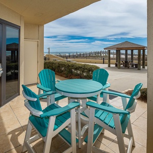 A cozy outdoor seating area features turquoise chairs and a round table, with a view of the surrounding beach access