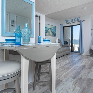 This bright and airy living area features a cozy seating space, a beach view, and a charming dining table with blue accents