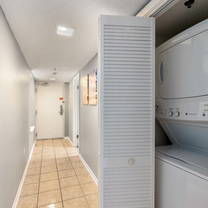 The hallway features a stacked washer and dryer tucked behind louvered doors, with tile flooring and light gray walls