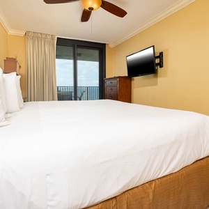 Cozy master bedroom featuring a plush king bed, flat-screen TV, and access to the beachfront balcony
