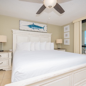 Brightly decorated master bedroom features a king bed, coastal artwork, and a balcony view of the gulf from the balcony