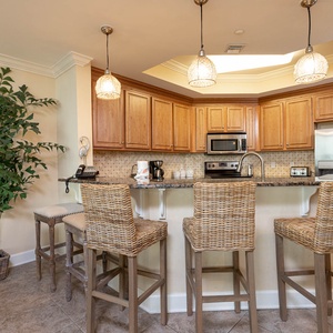 This kitchen features wood cabinetry, stainless appliances, and a breakfast bar with stylish wicker stools for casual dining