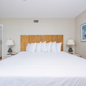 A king bed with a woven headboard is complemented by bedside lamps and framed artwork, creating a serene master bedroom
