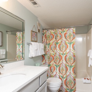 This bathroom features a vibrant shower curtain, a sleek vanity with a large mirror, and fresh towels for a refreshing stay