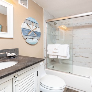 Brightly decorated guest bath featuring a sleek vanity, modern fixtures, and a glass-enclosed tub/shower combo for relaxation