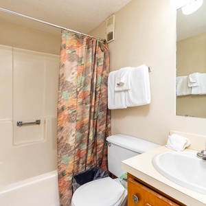 This bathroom features a clean, functional design with a shower, fresh towels, and a bright mirror for your convenience