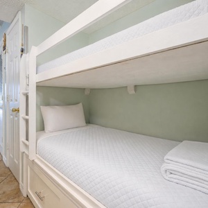 This cozy bunk area features white bedding and a playful sign, perfect for kids' adventures during their stay