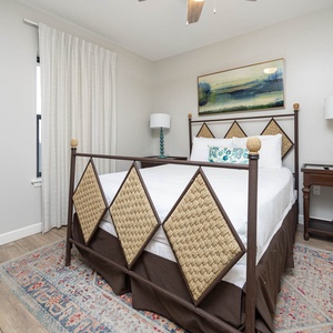 Relax in this charming guest bedroom featuring a decorative queen bed, colorful rug, and a bedside table with a stylish lamp