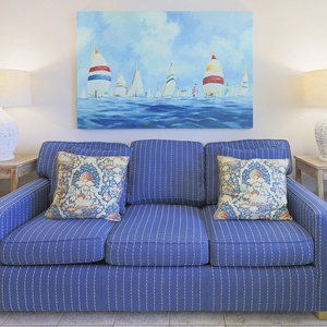 This living area features a cozy blue striped sofa adorned with decorative pillows and a vibrant sailing-themed artwork above