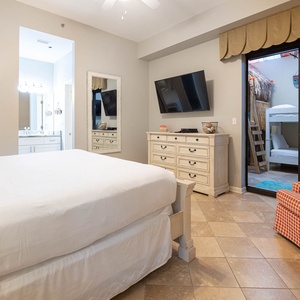 Master suite features a king bed, a TV, and a cozy chair, with a view of a bunk bed area in the indoor patio area
