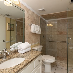The bathroom features a glass-enclosed walk-in shower, granite countertop, and neatly arranged white towels
