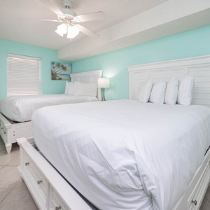 Bright guest bedroom featuring two queen beds, a flat-screen TV, and a serene aqua wall color with coastal artwork