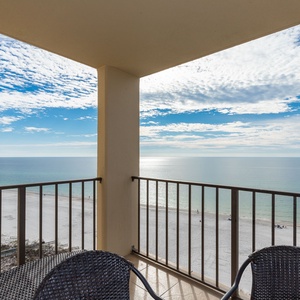 A spacious balcony offers a serene view of the tranquil waters and white sand beach, perfect for relaxation