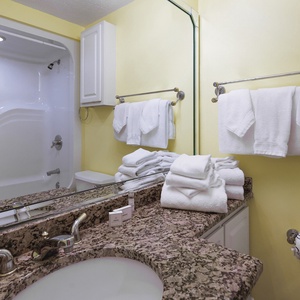 Bright yellow walls complement the granite countertop and fresh towels in this cheerful guest bath with a tub/shower combo