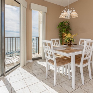 Bright dining area featuring a wooden table with white chairs, complemented by a vibrant floral centerpiece and beach views