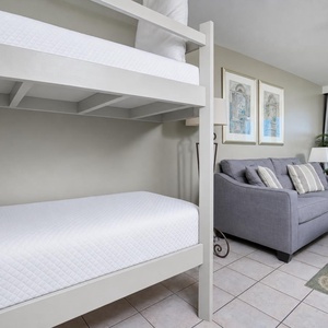 A cozy nook features a twin bunk bed and a sofa with queen sleeper, complemented by beach views through sliding glass doors
