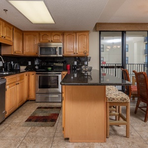 Modern kitchen features warm wood cabinetry, a breakfast bar with seating, and views of the gulf through large windows