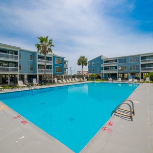 Relax by the sparkling pool surrounded by palm trees and charming beachside buildings for a perfect getaway experience