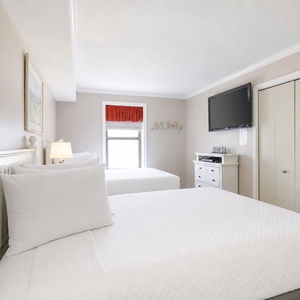 Bright guest bedroom featuring two queen beds, a flat-screen TV, and a window creating a cheerful vibe