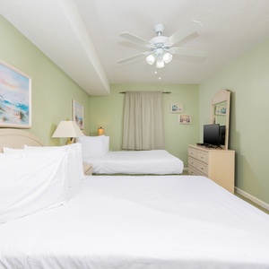 Guest room featuring two full beds, a light green accent wall, and a dresser with a TV, creating a relaxed atmosphere