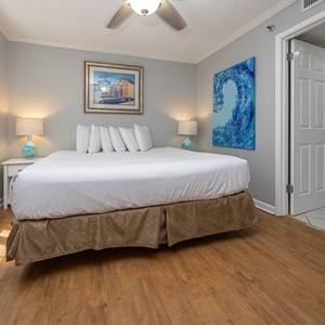 Brightly decorated guest bedroom featuring a king bed with plush pillows, coastal artwork, and natural light