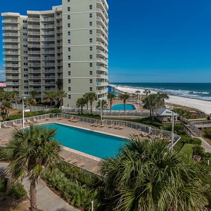 This inviting space features a stunning beachfront view, a sparkling pool below, and lush palm trees for a tropical getaway