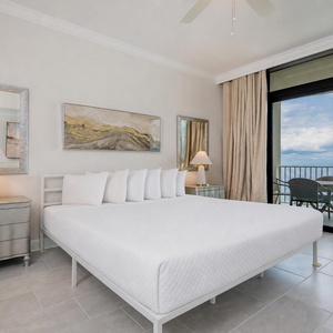Relax in this serene master bedroom featuring a king bed, elegant decor, and a beachfront balcony view