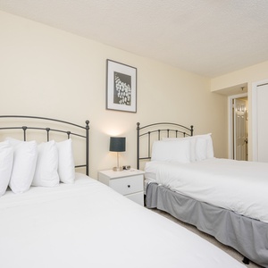 This guest bedroom features two metal-framed full beds, a nightstand with a lamp, and a neutral color scheme