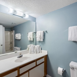 The guest bathroom features a light blue wall, a spacious vanity with neatly arranged towels, and a tub/shower combo